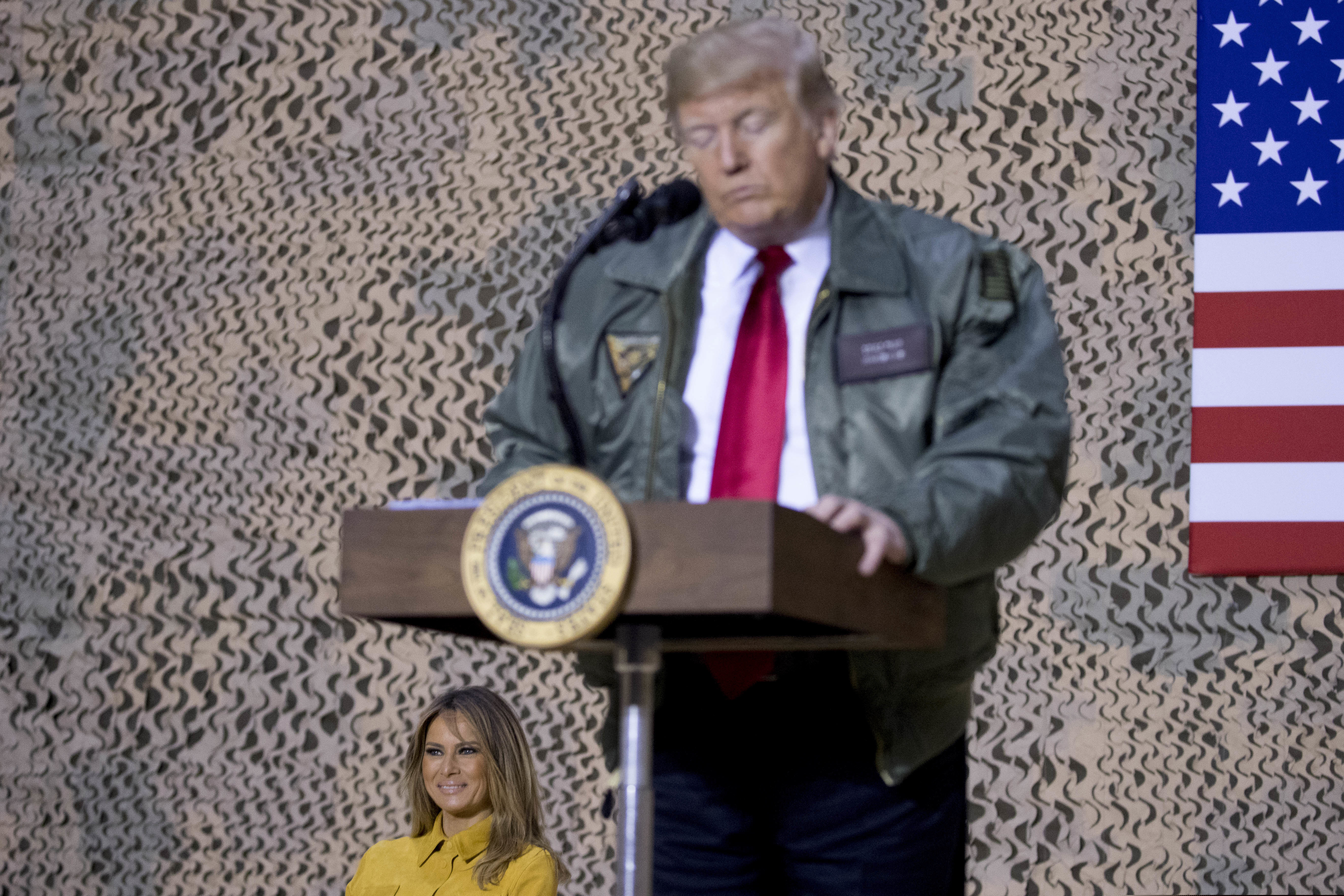 First lady Melania Trump, left, is seated on stage as President Donald Trump pauses as he speaks at a hangar rally at Al Asad Air Base, Iraq, Wednesday, Dec. 26, 2018. In a surprise trip to Iraq, President Donald Trump on Wednesday defended his decision to withdraw U.S. forces from Syria where they have been helping battle Islamic State militants. (AP Photo/Andrew Harnik)