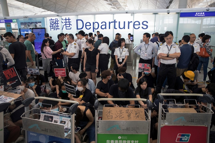 (Vincent Thian | AP Photo) Airport security personnel stand guard as travelers walk past protesters holding a sit-in rally at the departure gate of the Hong Kong International Airport in Hong Kong, Tuesday, Aug. 13, 2019. Protesters clogged the departure area at Hong Kong's reopened airport Tuesday, a day after they forced one of the world's busiest transport hubs to shut down entirely amid their calls for an independent inquiry into alleged police abuse.
