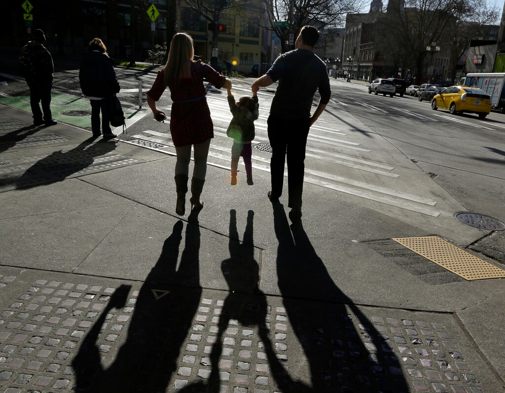 FILE - In this March 3, 2015, file photo, a child is lifted by her parents at a street corner in downtown Seattle. (AP Photo/Ted S. Warren, File)