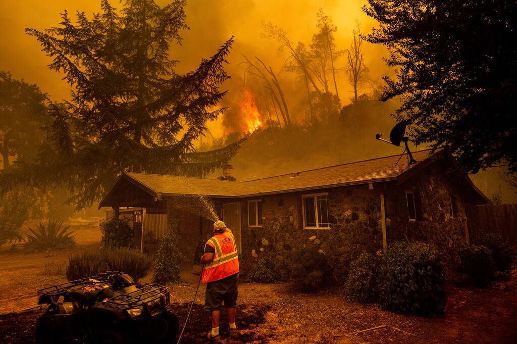 (Noah Berger | AP photo)
In this Aug. 18 photo, Jerry Kuny sprays water on a home as flames from the LNU Lightning Complex fires approach in unincorporated Napa County, Calif. This home remained standing as the main front passed although the fire went on to destroy multiple residences. With California fire crews strapped for resources as hundreds of lightning-sparked fires broke out in one night, crews of organized residents have worked to put out spot fires themselves in a massive complex of blazes along the central coast, banding together to sneak behind evacuation lines and keep properties safe.
