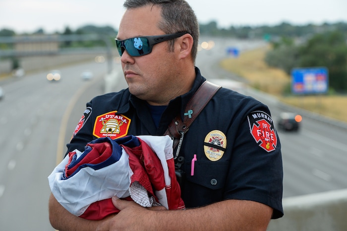 (Francisco Kjolseth  |  The Salt Lake Tribune)  Jason Hawkes with Murray Fire Tower 83, holds a flag to be unfurled over I-215 in Murray in anticipation of the arrival of the body of Utah firefighter Matt Burchett, 42, who died fighting a wildfire in California. Several firefighter details set up along the procession route after being flown in to the Utah Air National Guard in Salt Lake City on Wed. Aug. 15, 2018. The remains of the Draper battalion chief were transported to Jenkins-Soffe Mortuary in South Jordan.
