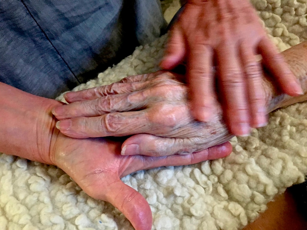 (Thomas Marrinson via AP) In this 2016 photo provided by Thomas Marrinson, Allison Beach holds the hand of her ailing mother Kathryne Beach inside her home in Hinesburg, Vt. Allison Beach and her husband struggled to figure out how to get help for her mother, who lived with them for three years before dying at their home Hinesburg, Vermont, in 2016. The experience led Beach, who was a nurse, to seek special training in end-of-life care and has become a doula, hoping to help others in such circumstances.