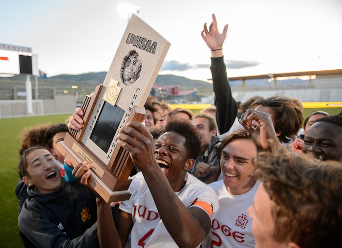 (Trent Nelson | The Salt Lake Tribune)  Judge Memorial players celebrate their win over Morgan High School in the 3A state championship game, Saturday May 12, 2018. Holding the trophy is Ferdinand Bambabate.