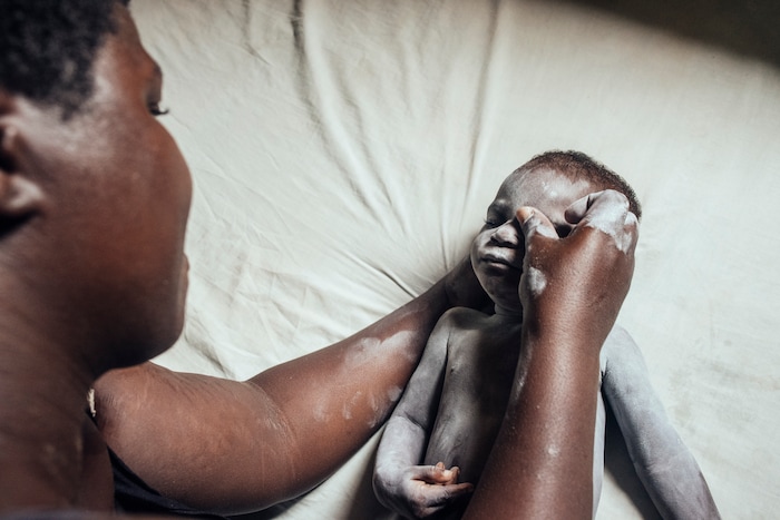 (KC Nwakalor | The New York Times) Faith Osi cares for her infant daughter, Miracle, after a bath on her family's cassava farm in Obrikom, in the heart of Nigeria's oil-rich delta, July 21, 2020. Around the world, the poor and marginalized are much more likely to be vulnerable to extreme heat; methane gas flares burning around the clock in Obrikom make this already hot area worse still.