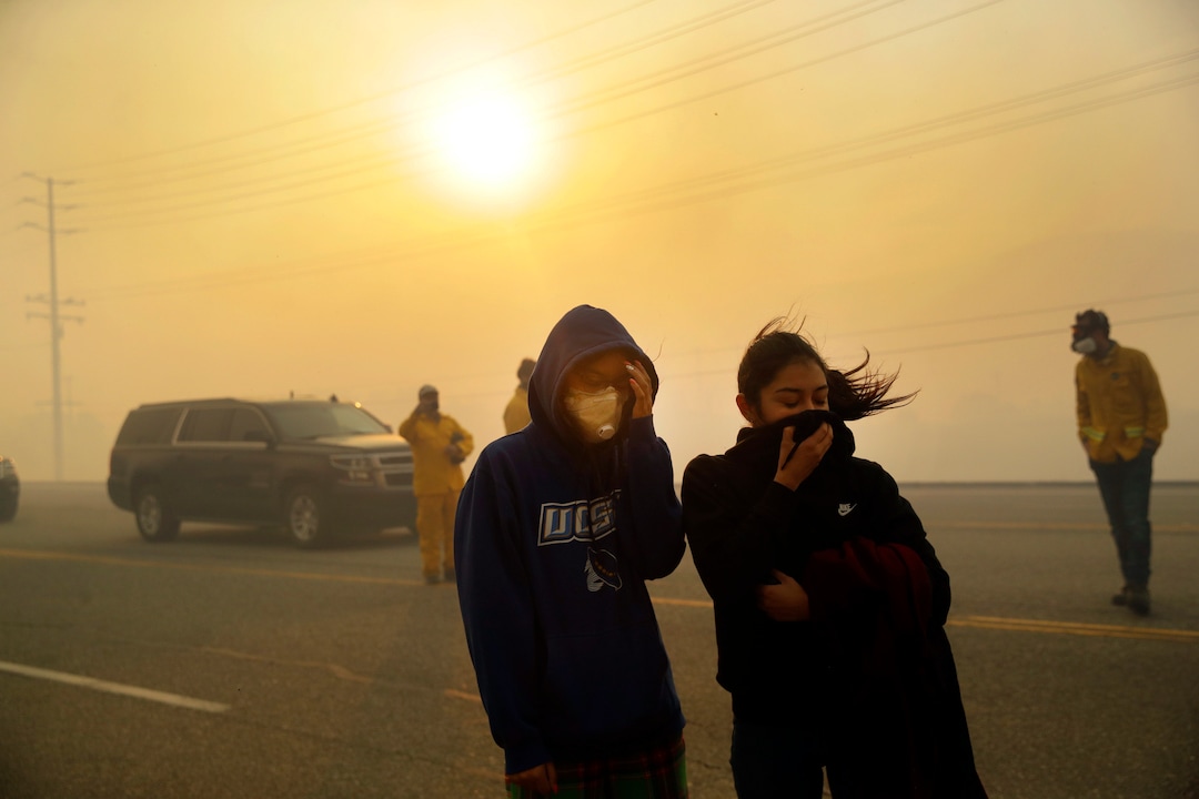 (Marcio Jose Sanchez | AP)  Natalie Acosta, left, and Lea Rivera cover their faces from the smoke created by the Easy Fire Wednesday, Oct. 30, 2019, in Simi Valley, Calif. Driven by powerful Santa Ana winds, the brush fire broke out before dawn between the cities of Simi Valley and Moorpark north of Los Angeles and exploded to more than 1,300 acres (526 hectares), threatening 6,500 homes, Ventura County officials said.