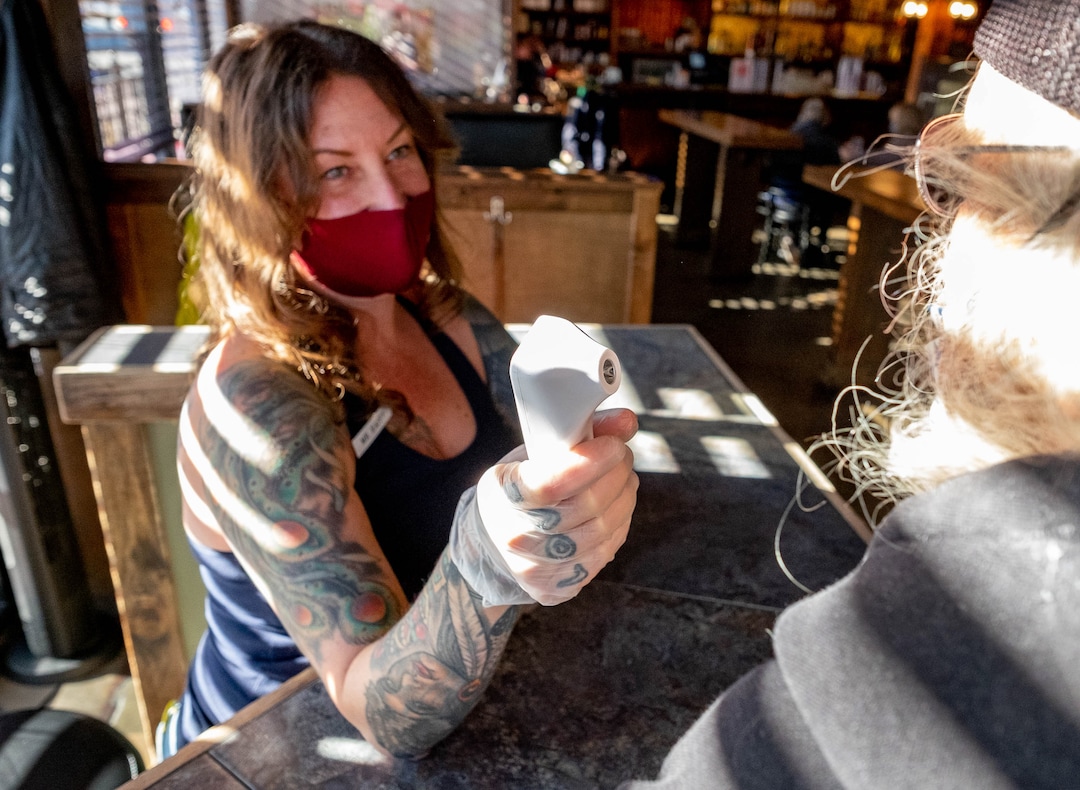 (Francisco Kjolseth  | The Salt Lake Tribune) Robin Brown checks the temperature of a patron entering the Green Pig Pub in Salt Lake City during the lunch hour on Thursday, Dec. 3, 2020. The owners of 25 different Utah bars — including the Green Pig Pub —  have sent a letter to Gov. Gary Herbert protesting the state health order that requires alcohol service to stop at 10 p.m They say the restriction is devastating the bar industry in Utah and has caused hundreds of thousands of dollars in lost  revenue, hurt employees, and could force many to close.