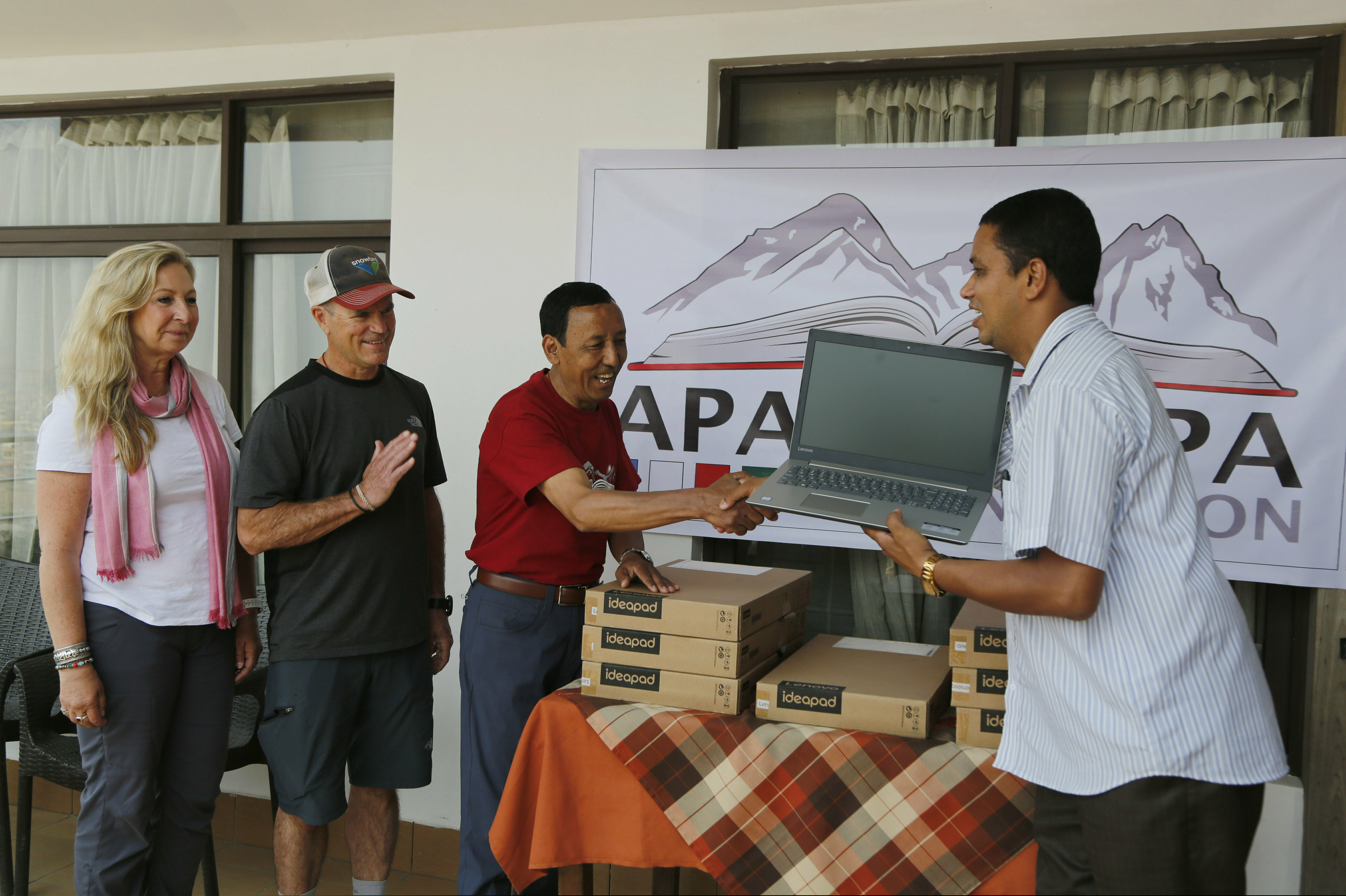 In this May 9, 2019, photo, Apa Sherpa, center, hands over a computer to Chakra Karki, representative of a school from Dhuske, Okhaldhunga district in Kathmandu, Nepal. Apa Sherpa has stood on top of the world more times than all but one other person. Now he wants to make sure no one feels compelled to follow in his footsteps. (AP Photo/Niranjan Shrestha)