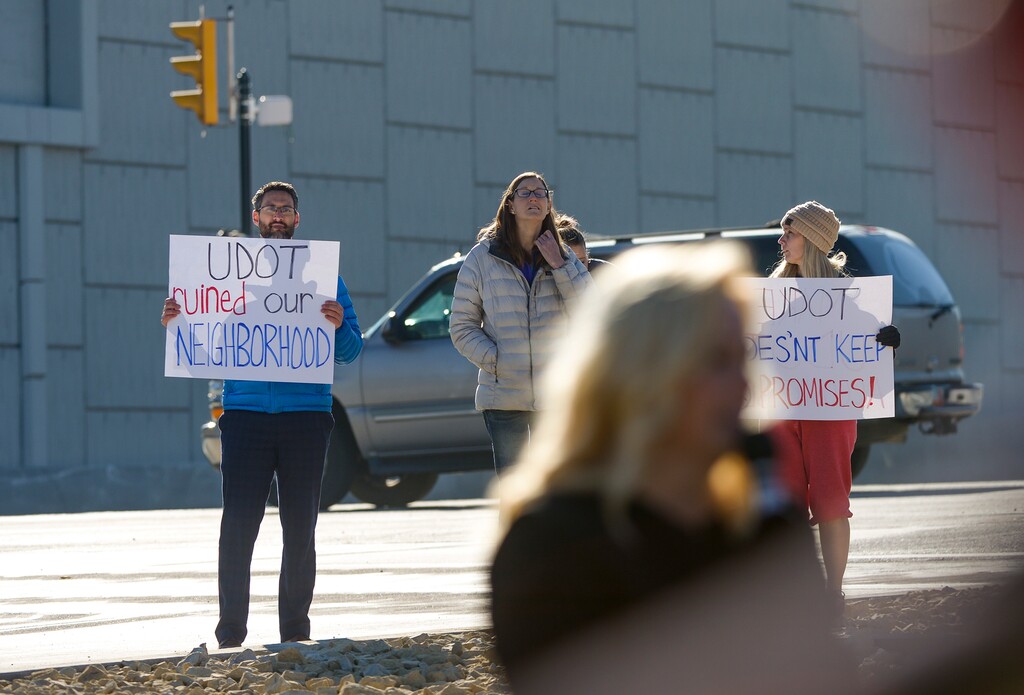 Leah Hogsten | The Salt Lake Tribune l-r Brent Jakobson, wife Elena Jakobson and Tiffany Skelton, who live on New Heritage Drive in West Jordan protested during a ceremony, Monday, Nov 19, 2018, celebrating completion of a $208 million project that converted four intersections into freeway-like interchanges at 5400 South, 7000 South, 9000 South and 11400 South. They complain that while a new sound wall being built at the 9000 South interchange will tower 11 feet above Bangerter, it will only be a couple of feet tall in their back yards which are at a much higher elevation — saying that creates a danger for children in the area, and also may not do much to reduce noise. Monday, Nov 19, 2018.