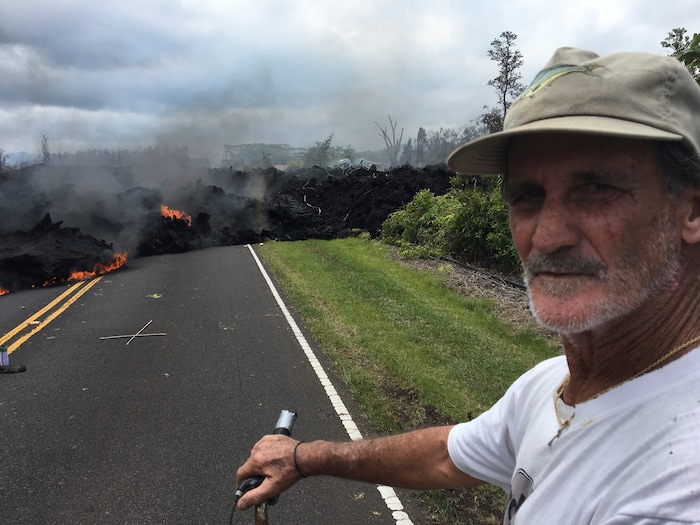 Resident Sam Knox, 65, rides his bicycle to the edge of the road as lava burns across the road in the Leilani Estates in Pahoa, Hawaii, Saturday, May 5, 2018. Hundreds of anxious residents on the Big Island of Hawaii hunkered down Saturday for what could be weeks or months of upheaval as the dangers from an erupting Kilauea volcano continued to grow. Lava spurted from volcanic vents, toxic gas filled the air and strong earthquakes, including a magnitude 6.9 temblor on Friday, rocked an already jittery population. (AP Photo/Marco Garcia)