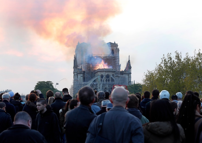 People watch as flames and smoke rise from Notre Dame cathedral as it burns in Paris, Monday, April 15, 2019. Massive plumes of yellow brown smoke is filling the air above Notre Dame Cathedral and ash is falling on tourists and others around the island that marks the center of Paris. (AP Photo/Thibault Camus)