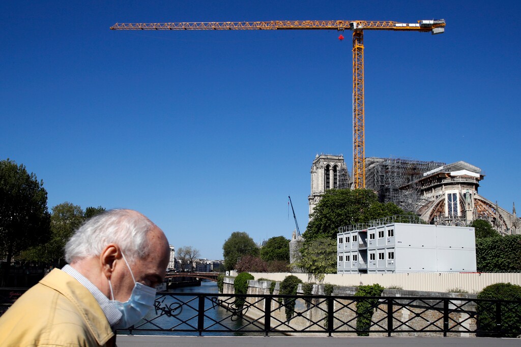 FILE - In this Tuesday, April 14, 2020 file photo, a man wearing face mask walks past Notre Dame Cathedral in Paris. Officials say restorers at Paris’ fire-damaged Notre Dame cathedral have completed key preliminary work by successfully removing all the perilous roof scaffolding. It was thought that the scaffolding might have melded to the cathedral in the fire, and be keeping it in place. When the Notre Dame fire broke out on April 15 last year destroying the spire, the cathedral was already under restoration. The scaffolding previously installed resisted collapse, “but was deformed by the heat of the fire” Notre Dame restoration officials said in a communique. (AP Photo/Christophe Ena, File)