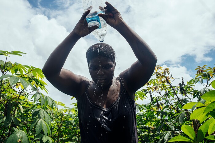 (KC Nwakalor | The New York Times) Faith Osi pours water on her head to cool down while working on her family's cassava farm in Obrikom, in the heart of Nigeria's oil-rich delta, July 21, 2020. Around the world, the poor and marginalized are much more likely to be vulnerable to extreme heat; methane gas flares burning around the clock in Obrikom make this already hot area worse still.