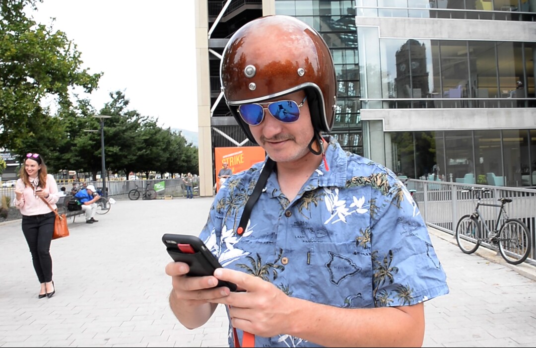 (Rick Egan  |  The Salt Lake Tribune)      Salt Lake Tribune columnist Robert Gehrke searches for a Lime Scooter at the start of a downtown transportation race from Library Square to the Tribune building at the Gateway on Thursday, Aug. 2, 2018. Modes of transportation included, rentable electric scooters, Green Bike, TRAX, Lyft, and walking.