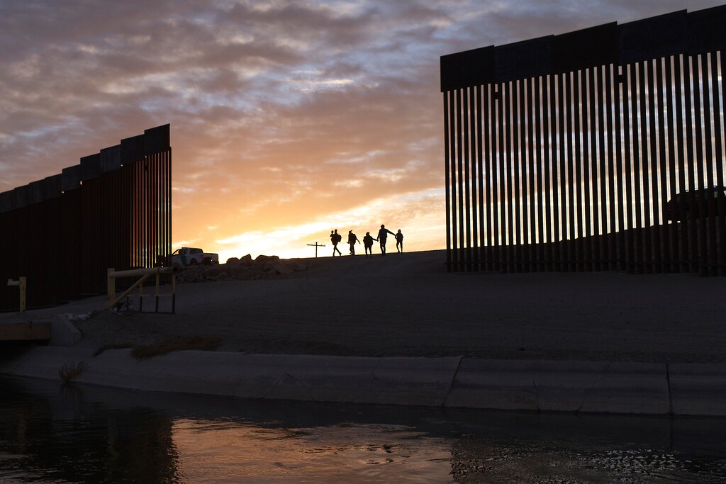 (Eugene Garcia | AP) A pair of migrant families from Brazil passes through a gap in the border wall to reach the United States after crossing from Mexico in Yuma, Ariz., to seek asylum on June 10, 2021.