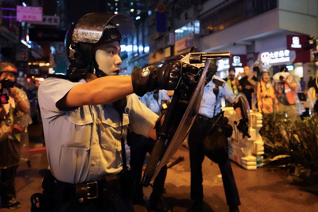 (AP Photo/Vincent Yu) A policeman points a weapon during a protest in Hong Kong, Sunday, Aug. 25, 2019. Hong Kong police have rolled out water cannon trucks for the first time in this summer's pro-democracy protests. The two trucks moved forward with riot officers Sunday evening as they pushed protesters back along a street in the outlying Tsuen Wan district.