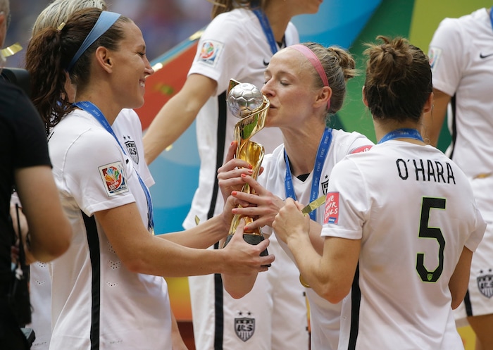 United States' Becky Sauerbrunn kisses the trophy as Lauren Holiday, left, and Kelley O'Hara, right, look on after the U.S. beat Japan 5-2 in the FIFA Women's World Cup soccer championship in Vancouver, British Columbia, Canada, Sunday, July 5, 2015. (AP Photo/Elaine Thompson)