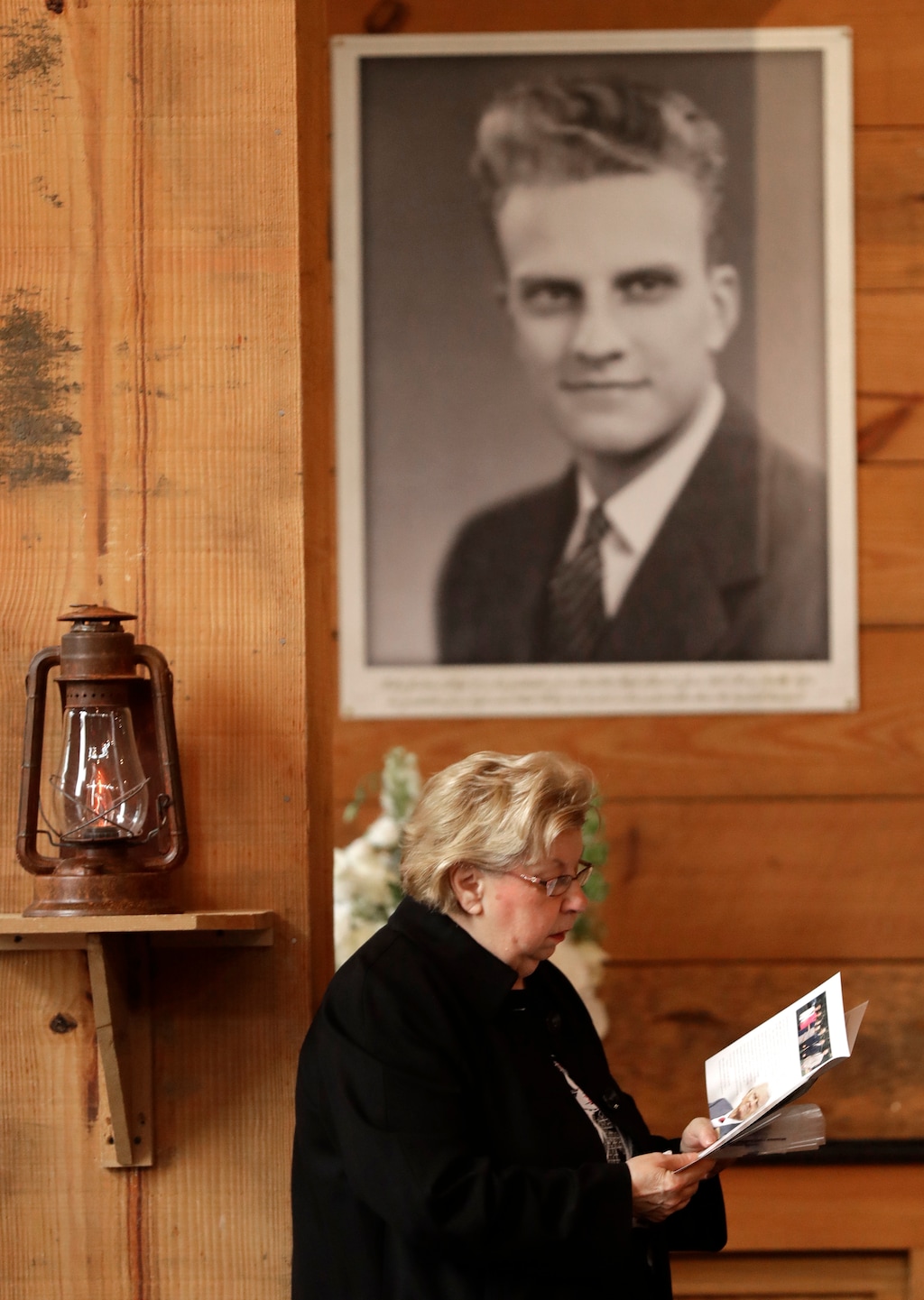 A woman reads a brochure under a large photo of Billy Graham as she pays respects to Billy Graham during a public viewing at the Billy Graham Library in Charlotte, N.C., Monday, Feb. 26, 2018. (AP Photo/Chuck Burton)