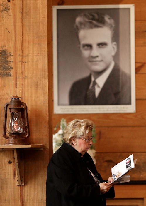 A woman reads a brochure under a large photo of Billy Graham as she pays respects to Billy Graham during a public viewing at the Billy Graham Library in Charlotte, N.C., Monday, Feb. 26, 2018. (AP Photo/Chuck Burton)