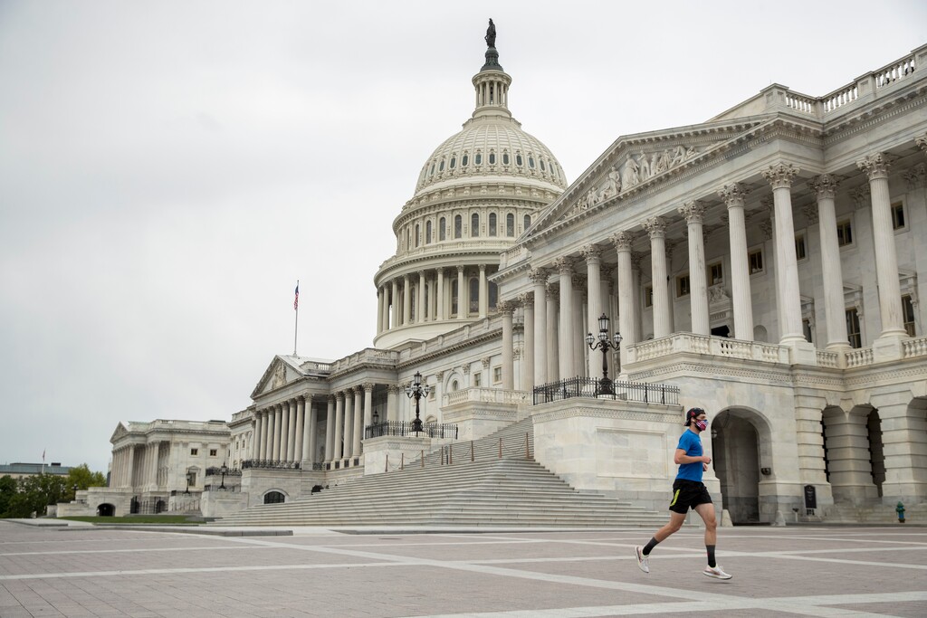 A man wearing a mask depicting American flags jogs past the U.S. Capitol Building, Tuesday, April 28, 2020, in Washington. The U.S. House of Representatives has canceled plans to return next week, a reversal after announcing it a day earlier. (AP Photo/Andrew Harnik)