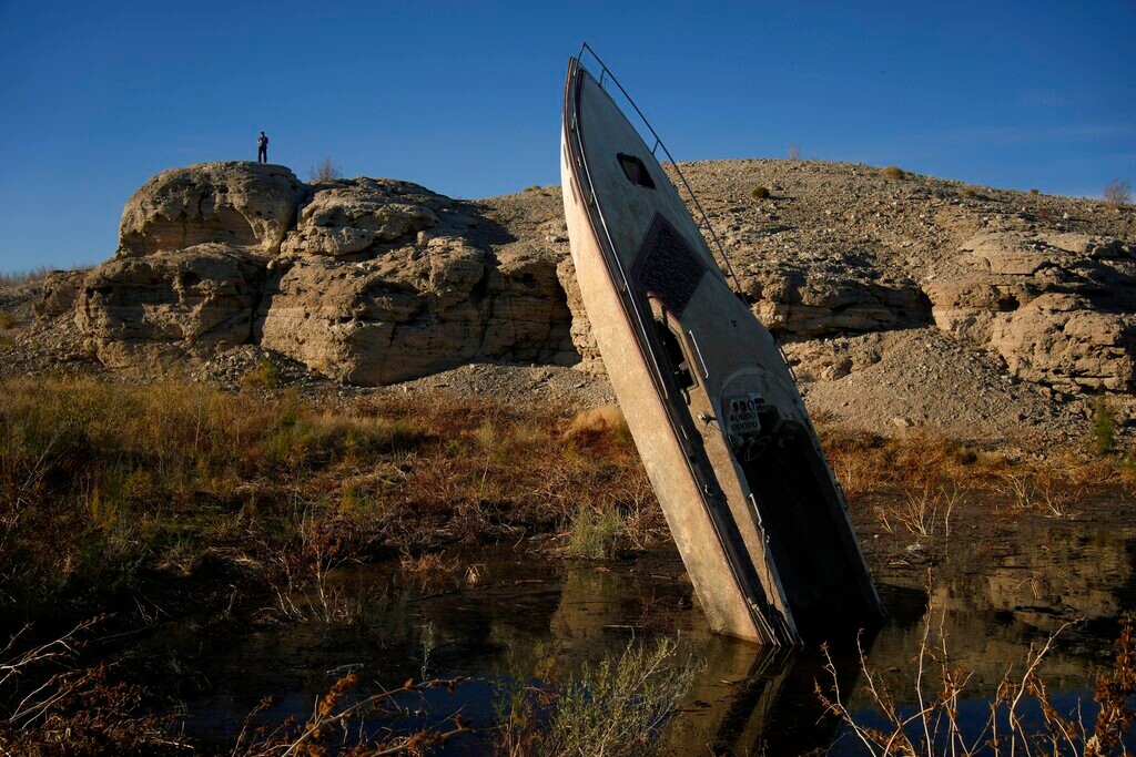(John Locher | AP) A man stands on a hill overlooking a formerly sunken boat standing upright into the air with its stern buried in the mud along the shoreline of Lake Mead at the Lake Mead National Recreation Area, Friday, Jan. 27, 2023, near Boulder City, Nev.