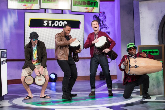 (Photo courtesy of truTV) Host Michael Torpey drums with contestants on the set of "Paid Off."