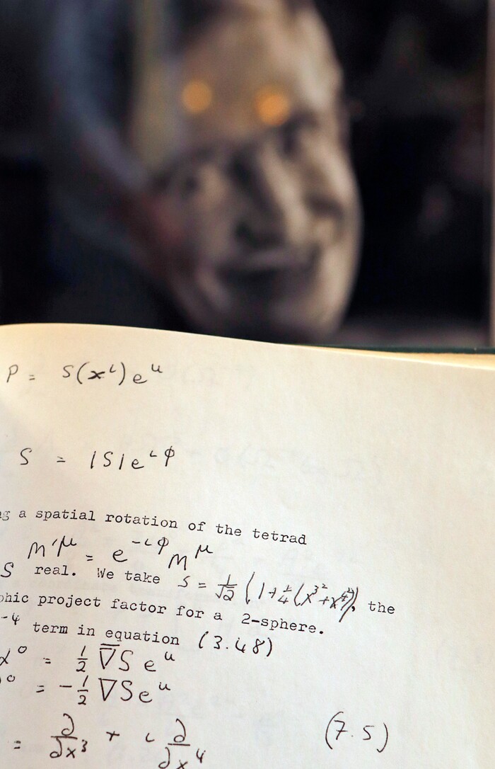 A Book, written and corrected with handwritten annotation by Stephen Hawking is one of the personal and academic possessions of Stephen Hawking, photo behind, on display at the auction house Christies in London, Friday, Oct. 19, 2018. The online auction announced Monday Oct. 22, 2018, by auctioneer Christie’s features 22 items from Hawking, including his doctoral thesis on the origins of the universe, with the sale scheduled for 31 October and 8 November. (AP Photo/Frank Augstein)