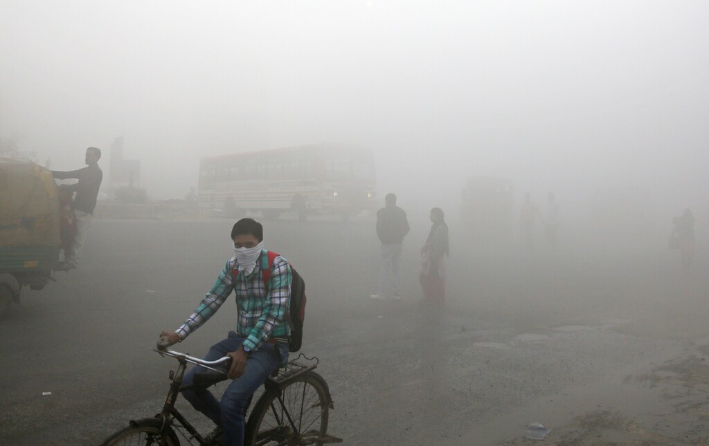 FILE - In this Nov. 10, 2017 file photo, Indian commuters wait for transport amid a thick blanket of smog on the outskirts of New Delhi, India. The petroleum coke being burned in countless factories and plants is contributing to dangerously filthy air in India, which already has many of the world's most polluted cities. India's energy-hungry industries like petcoke because it's cheaper and burns hotter than coal; they also defend their use by saying they're recycling a waste that's being produced anyway. (AP Photo/Altaf Qadri, File)