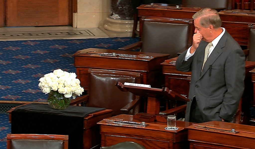In this image from Senate Television, Sen. Lindsey Graham, R-S.C., pauses as he speaks on the Senate floor at the Capitol in Washington, on Tuesday, Aug. 28, 2018, next to the desk of Sen. John McCain, R-Ariz., draped in black with a bowl of white roses sitting on it. McCain died on Aug. 25 after battling brain cancer. Graham was McCain's best friend in the Senate. (Senate Television via AP)