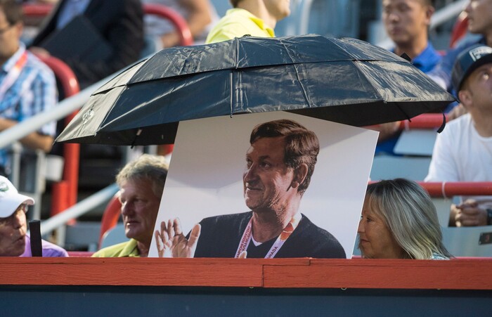 Fans hold an umbrella over a photo of hockey great Wayne Gretzky during a rain-delayed quarterfinal match between Denis Shapovalov, of Canada, and Adrian Mannarino, of France, at the Rogers Cup tennis tournament Friday, Aug.11, 2017, in Montreal. (Paul Chiasson/The Canadian Press via AP)