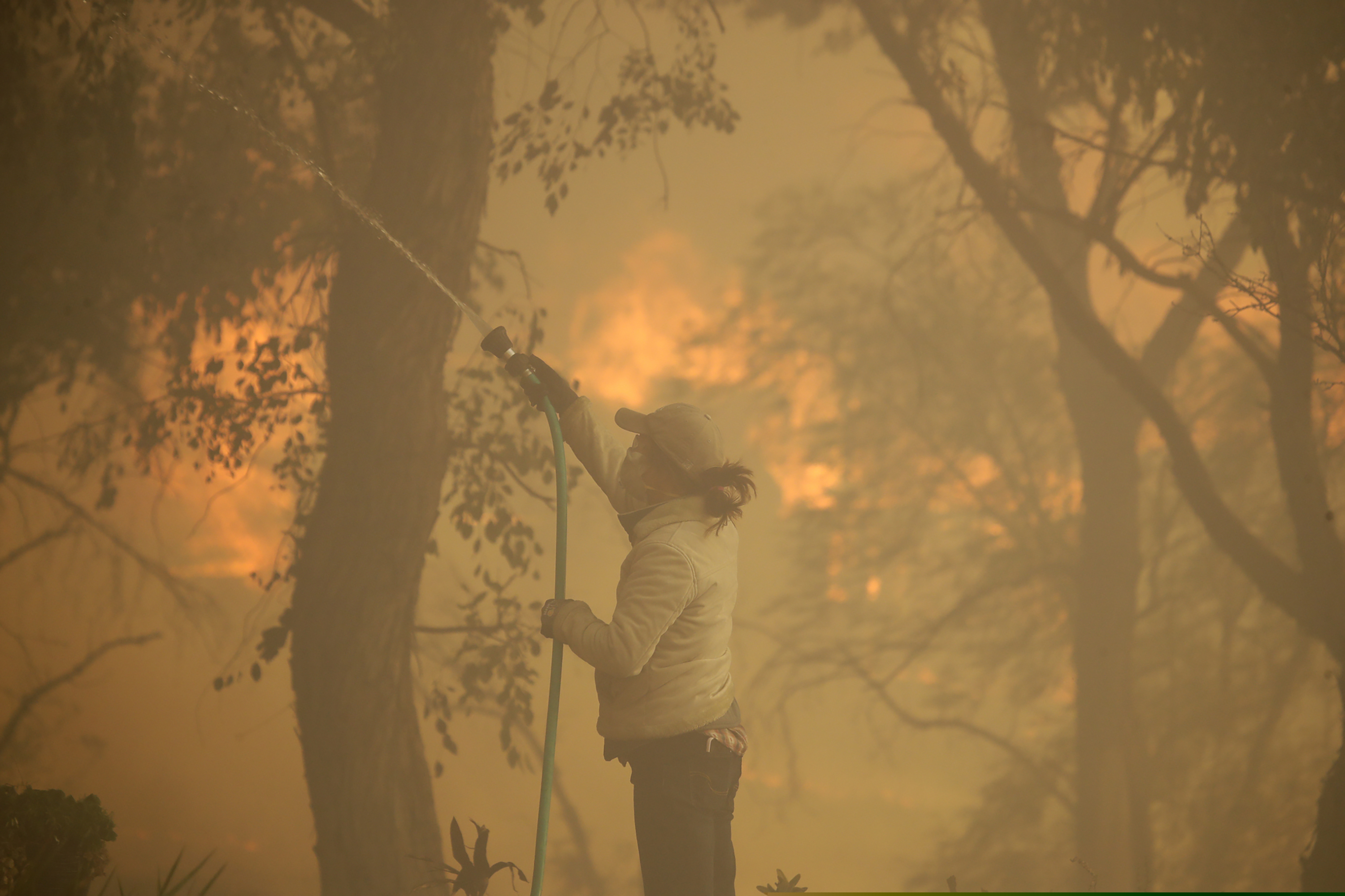 (Marcio Jose Sanchez | AP) Beth Rivera hoses down her property as the Easy fire approaches Wednesday, Oct. 30, 2019, in Simi Valley, Calif.  Driven by powerful Santa Ana winds, the brush fire broke out before dawn between the cities of Simi Valley and Moorpark north of Los Angeles and exploded to more than 1,300 acres (526 hectares), threatening 6,500 homes, Ventura County officials said.