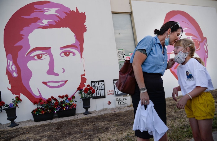 (Francisco Kjolseth  |  The Salt Lake Tribune) Tiffany James kisses her daughter Ruby, 7, as they visit the portrait of their son and brother Zane James who was killed by Cottonwood Heights police in 2018, as people gather for a vigil on the six-year anniversary of Dillon Taylor’s death by the murals of those people killed by police near 800 South and 300 West in Salt Lake City on Tuesday, August 11, 2020. Multiple families who’s loved one’s are depicted on the walls joined the vigil as they moved from portrait to portrait to remember them.