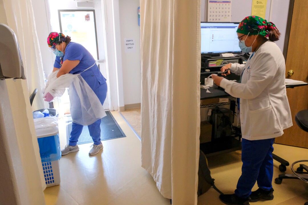 (Leah Hogsten  |  The Salt Lake Tribune) Navajo Mountain Health Clinic medical assistant Toni Black strips off her personal protective equipment, left, as lab technician Roxanna Yazzie tests bloodwork from a 74-year-old Diné patient, Aug., 25, 2020. Yazzie is one of ten staff members responsible for driving coronavirus tests from Utah’s Navajo Mountain to the San Juan County Public Health building in Blanding, a 185 mile trip one-way.