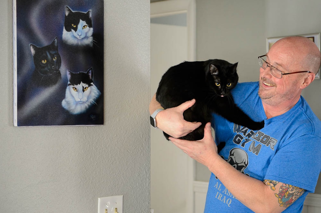 (Trent Nelson | The Salt Lake Tribune)  Jim Vesock with one of his pet cats, Raidan, in West Valley City on Wednesday March 13, 2019. The painting at left depicts three of his previous cats.