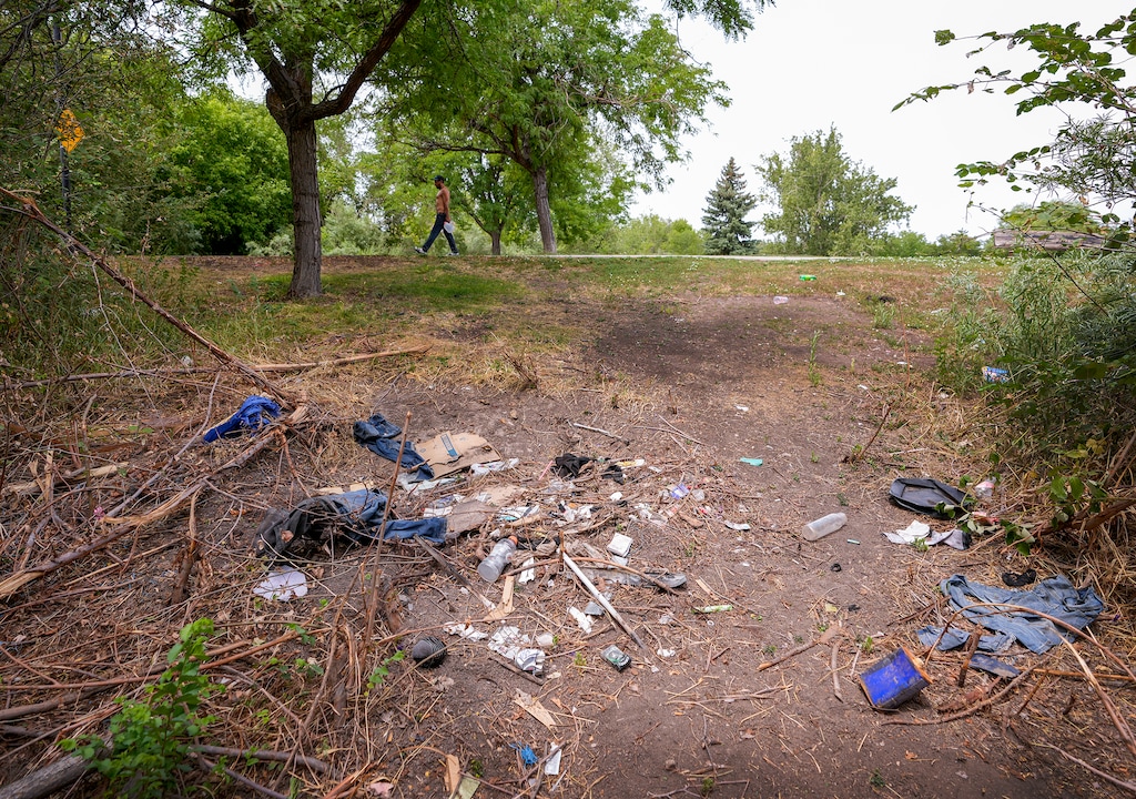 (Leah Hogsten | The Salt Lake Tribune) A man carrying jugs of water walks past trash strewn along the bank of the Jordan River near Cottonwood Park in 2022. Salt Lake City is closing part of the Jordan River Trail near the park.