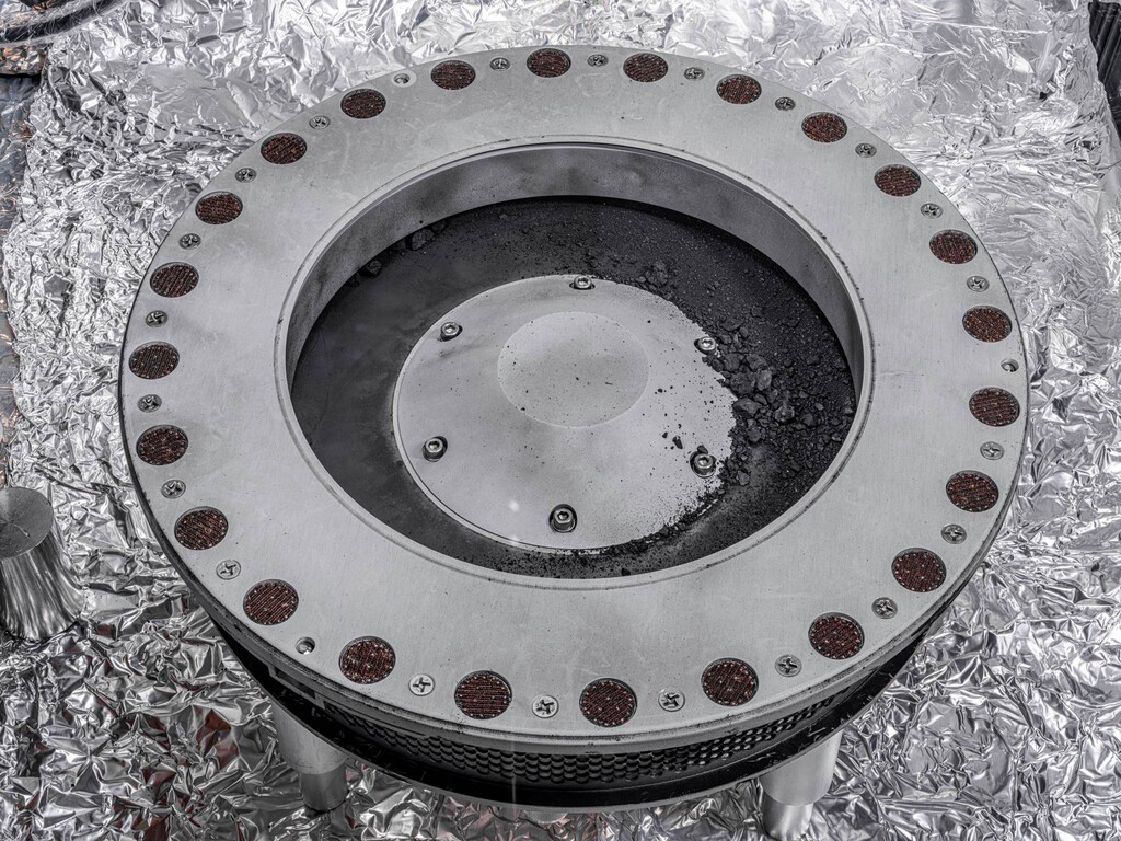 (Erika Blumenfeld, Joseph Aebersold | NASA via AP) This photo provided by NASA on Wednesday, Oct. 11, 2023 shows the outside of the OSIRIS-REx sample collector with material from asteroid Bennu at middle right. Scientists have found evidence of both carbon and water in initial analysis of this material. The bulk of the sample is located inside.