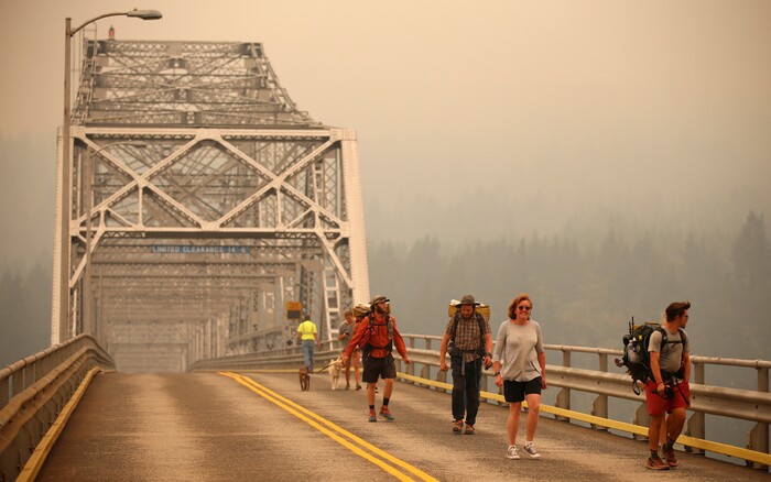 Pedestrians walk off the Bridge of the Gods, which spans the Columbia River between Washington and Oregon states, as smoke from the Eagle Creek wildfire obscures the Oregon hills in the background near Stevenson, Wash., Wednesday, Sept. 6, 2017. The Eagle Creek fire continues to burn on the Oregon side of the river near the town of Cascade Locks, Ore. Officials closed the bridge to pedestrians and onlookers after this photo was taken. (AP Photo/Randy L. Rasmussen)