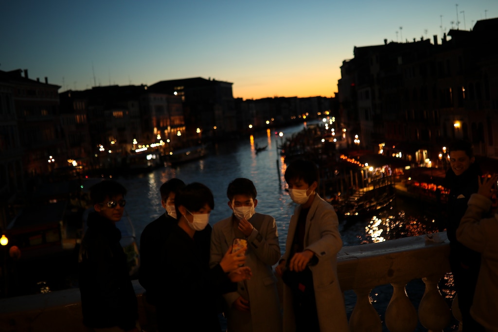 (Francisco Seco | AP) Tourists wearing protective masks pose for a photograph at the Rialto bridge as the sun sets in Venice, Italy, Friday, Feb. 28, 2020. Authorities in Italy decided to re-open schools and museums in some of the areas less hard-hit by the coronavirus outbreak in the country which has the most cases outside of Asia, as Italians on Friday yearned for a return to normal life even amid fears that the outbreak could plunge the country's economy into recession.