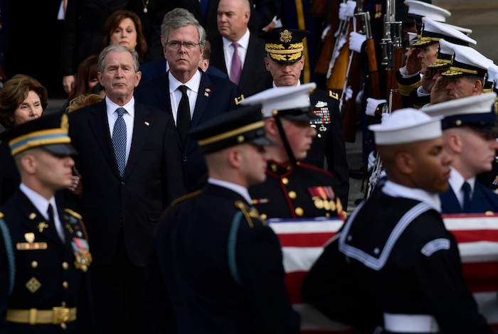 Former President George W. Bush, flanked by his wife Laura Bush, left, and brother former Florida Gov. Jeb Bush, watch as the casket of former President George H.W. Bush is carried out after a State Funeral at the National Cathedral in Washington, Wednesday, Dec. 5, 2018. (AP Photo/Susan Walsh)