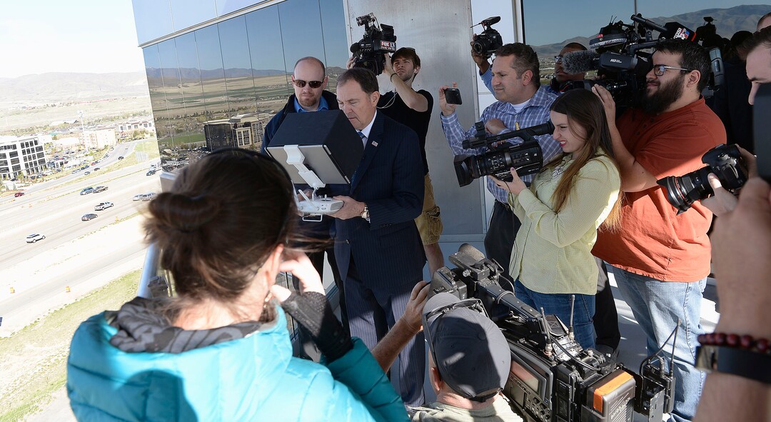 (Al Hartmann  |  The Salt Lake Tribune) 	News photographers surround Gov. Gary R. Herbert, center, as he uses remote control to pilot a drone in Lehi Wednesday April 25 to get a view of  the Utah Department of Transportation’s (UDOT) I-15 Tech Corridor project in Lehi for a pre-construction site tour. The project will widen I-15 with two new lanes in each direction from Lehi Main Street to S.R. 92. It will also alleviate east-west congestion in this busy area by building a bridge at Triumph Boulevard, adding a one-way frontage road system from 2100 North to S.R. 92 and reconstructing those two interchanges. In addition, the project will construct 17 bridges and include several bike and pedestrian improvements.  