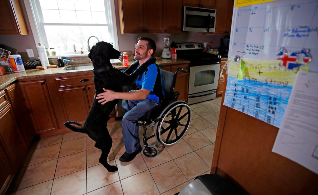 In this April 4, 2018, photo, Boston Marathon bombing survivor Marc Fucarile pats his dog Onyx at his home in Reading, Massachusetts. The 39-year-old from the Boston area lost his right leg in the blast, and his badly maimed left leg causes him unceasing pain. He fears another amputation might be his only option.  (AP Photo/Charles Krupa)