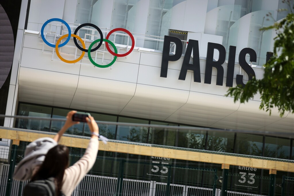 (Thomas Padilla | AP) A woman takes a photograph of the Paris La Defense Arena, Wednesday, June 12, 2024 in Nanterre, outside Paris. The Paris La Defense Arena will host the swimming and some water polo events during the Paris 2024 Olympic Games.
