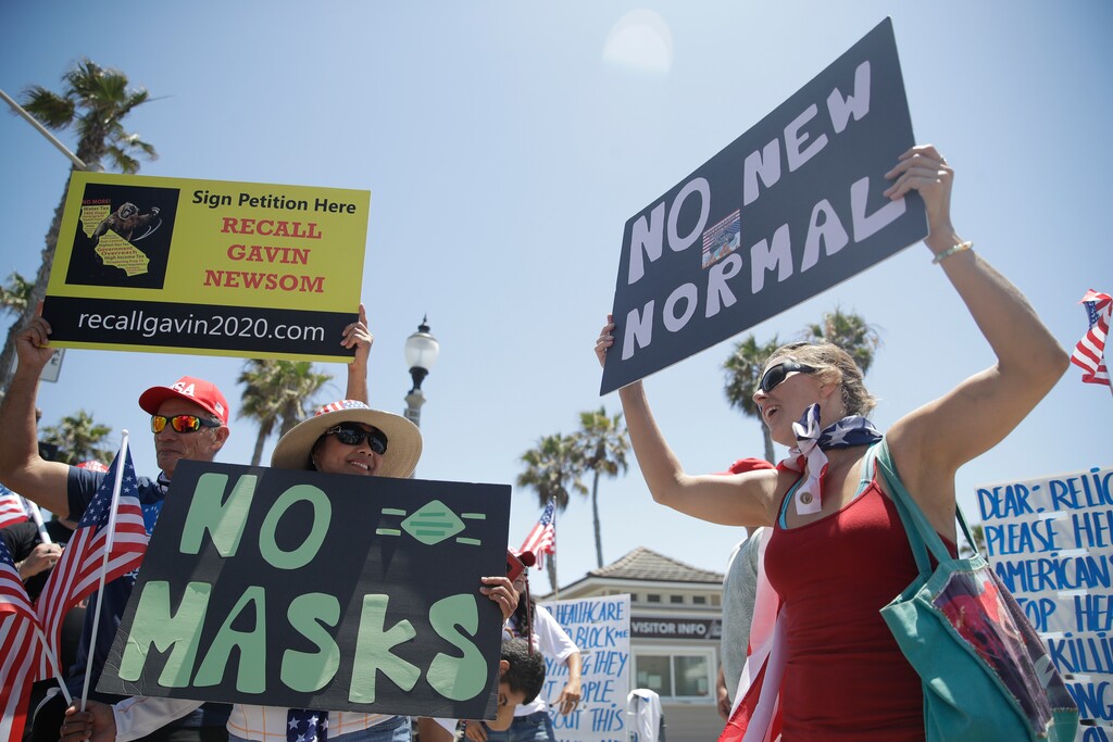 (Marcio Jose Sanchez | AP file photo)  Demonstrators hold signs as they protest the lockdown and wearing masks Saturday, June 27, 2020, in Huntington Beach, Calif.