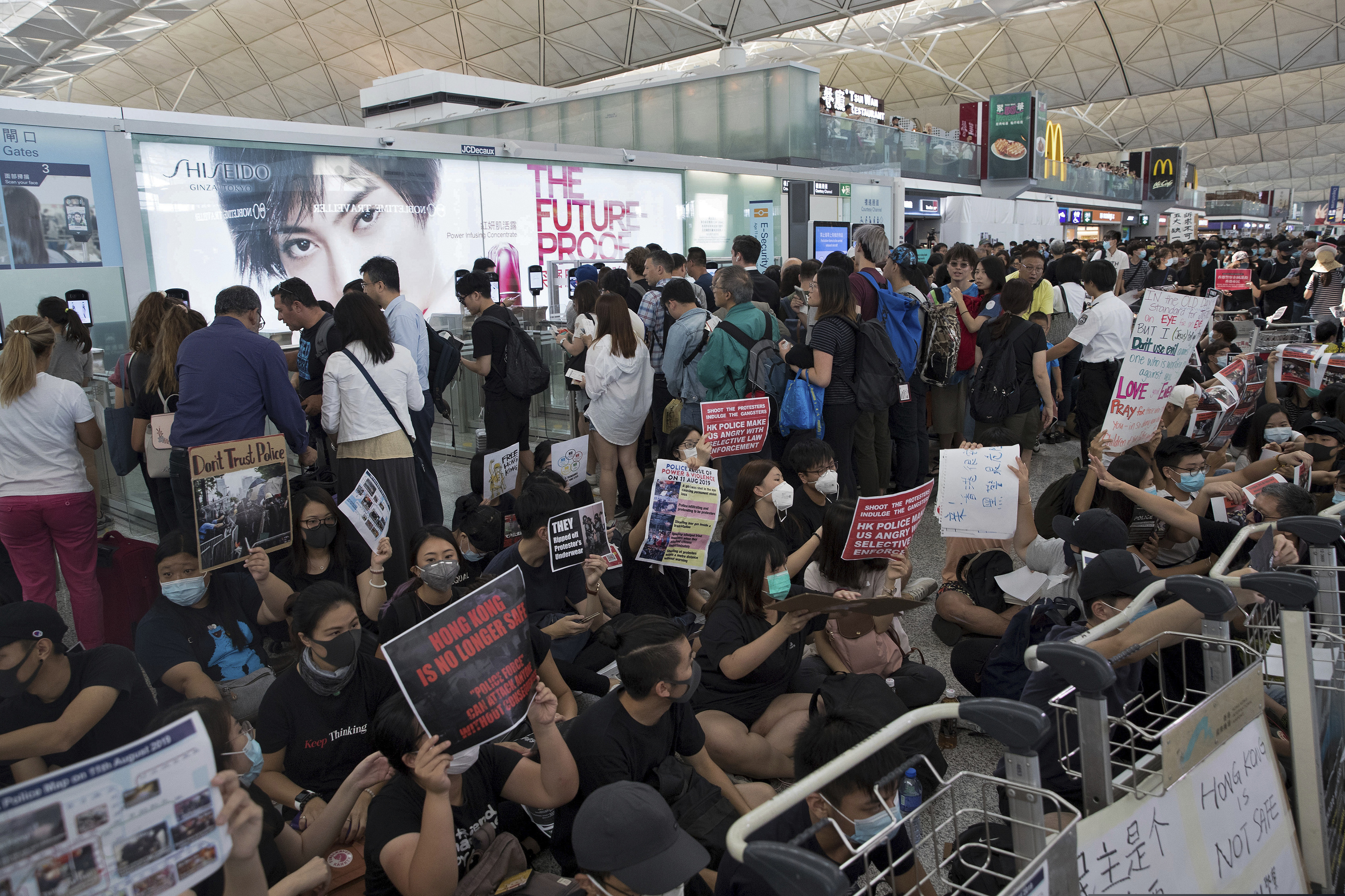 (Vincent Thian | AP Photo) Travelers walk past as protesters hold a sit-in rally near the departure gate of the Hong Kong International Airport in Hong Kong, Tuesday, Aug. 13, 2019. Protesters clogged the departure area at Hong Kong's reopened airport Tuesday, a day after they forced one of the world's busiest transport hubs to shut down entirely amid their calls for an independent inquiry into alleged police abuse.