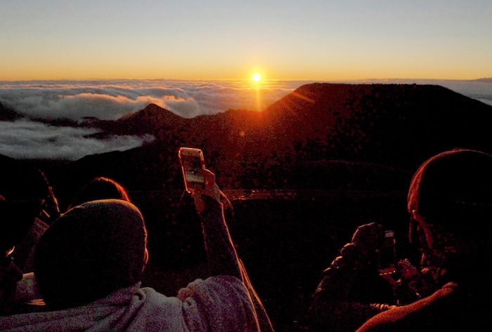 FILE - In this Jan. 22, 2017 file photo, people watch as the sun rises in front of the summit of Haleakala volcano in Haleakala National Park on Hawaii's island of Maui. Hawaii residents and an organization representing federal workers filed a lawsuit against the Federal Aviation Administration on Wednesday, Oct. 4, 2017 seeking to force it to do something about tour helicopters buzzing around seven national parks across the country. (AP Photo/Caleb Jones, File)