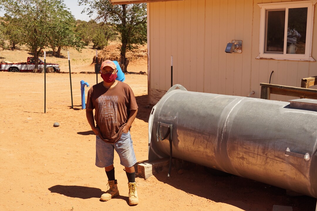 (Zak Podmore | The Salt Lake Tribune) Harrison Ross, one of the beneficiaries of the DigDeep Navajo Mountain Program, stands beside the steel tank he used to fill with water hauled by pickup truck. The blue piping connects with the underground cistern installed by DigDeep in 2019.