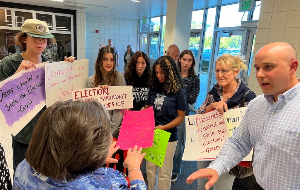 (Bryan Schott | The Salt Lake Tribune) Protesters at Highland High School Monday night hold signs highlighting social media posts from Republican county clerk candidate Goud Maragani, who has claimed the 2020 election was stolen. Maragani walked back those comments during a candidate forum on Monday.