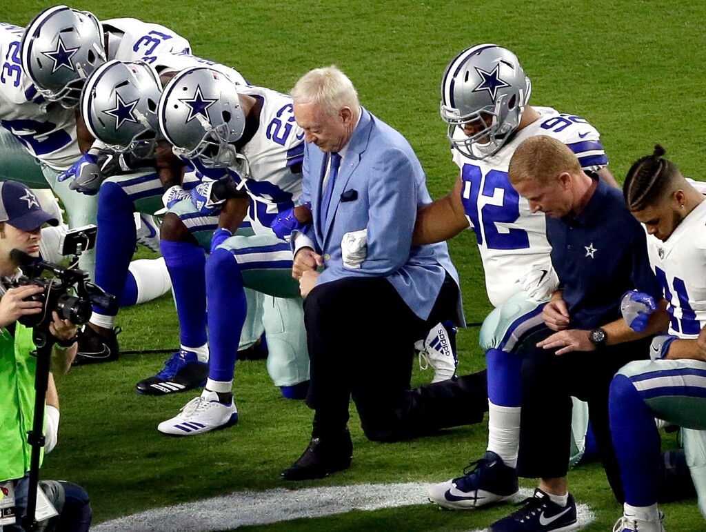 FILE - In this Monday, Sept. 25, 2017 file photo, the Dallas Cowboys, led by owner Jerry Jones, center, take a knee prior to the national anthem prior to an NFL football game against the Arizona Cardinals, in Glendale, Ariz. President Donald Trump's clash with the scores of professional football players who knelt during the Star Spangled Banner last weekend has set off a heated debate over proper etiquette during the national anthem. But throughout the world, flags, anthems and other national symbols can often divide as much as they unify, especially in countries with large religious or ethnic divisions. (AP Photo/Matt York, File)
