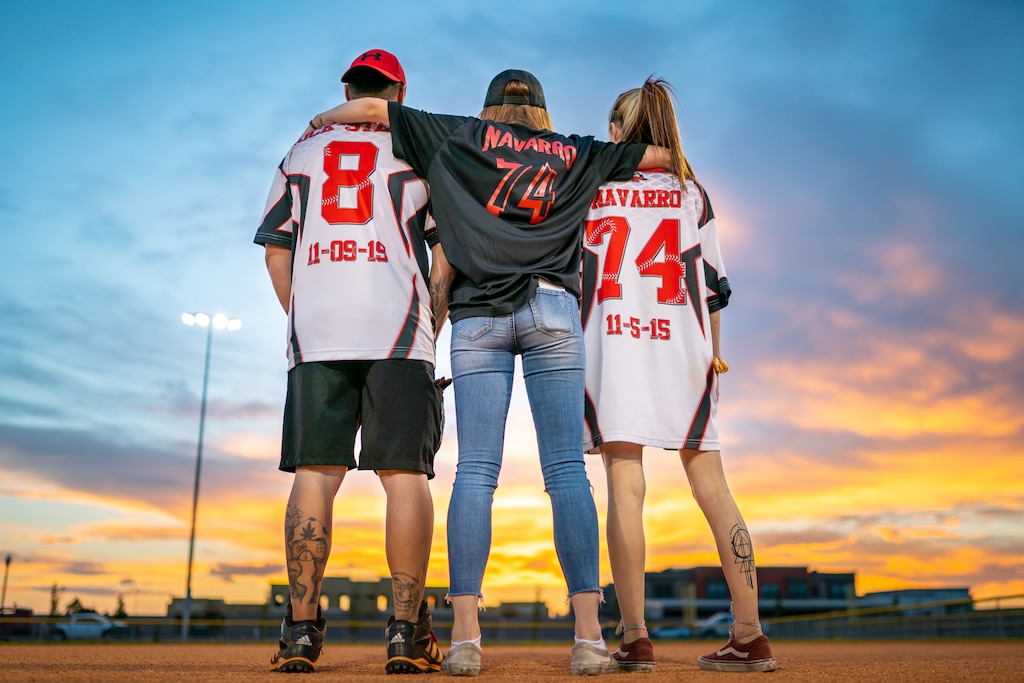 (Ranger Peterson) Friends and family pay tribute to Aaron Navarro at a fundraiser softball tournament on Sept. 10, 2021, less than a week after Navarro died from COVID-19 in St. George. Navarro and Nathan Spendlove, left, have long been instrumental in addiction recovery support groups and sports leagues in southwest Utah. Navarro's daughters, Dallas and Saleena Navarro, center and right, wear their father's jersey in his honor. The dates on the shirts signify a sobriety "birthday," or the date when recovery began.