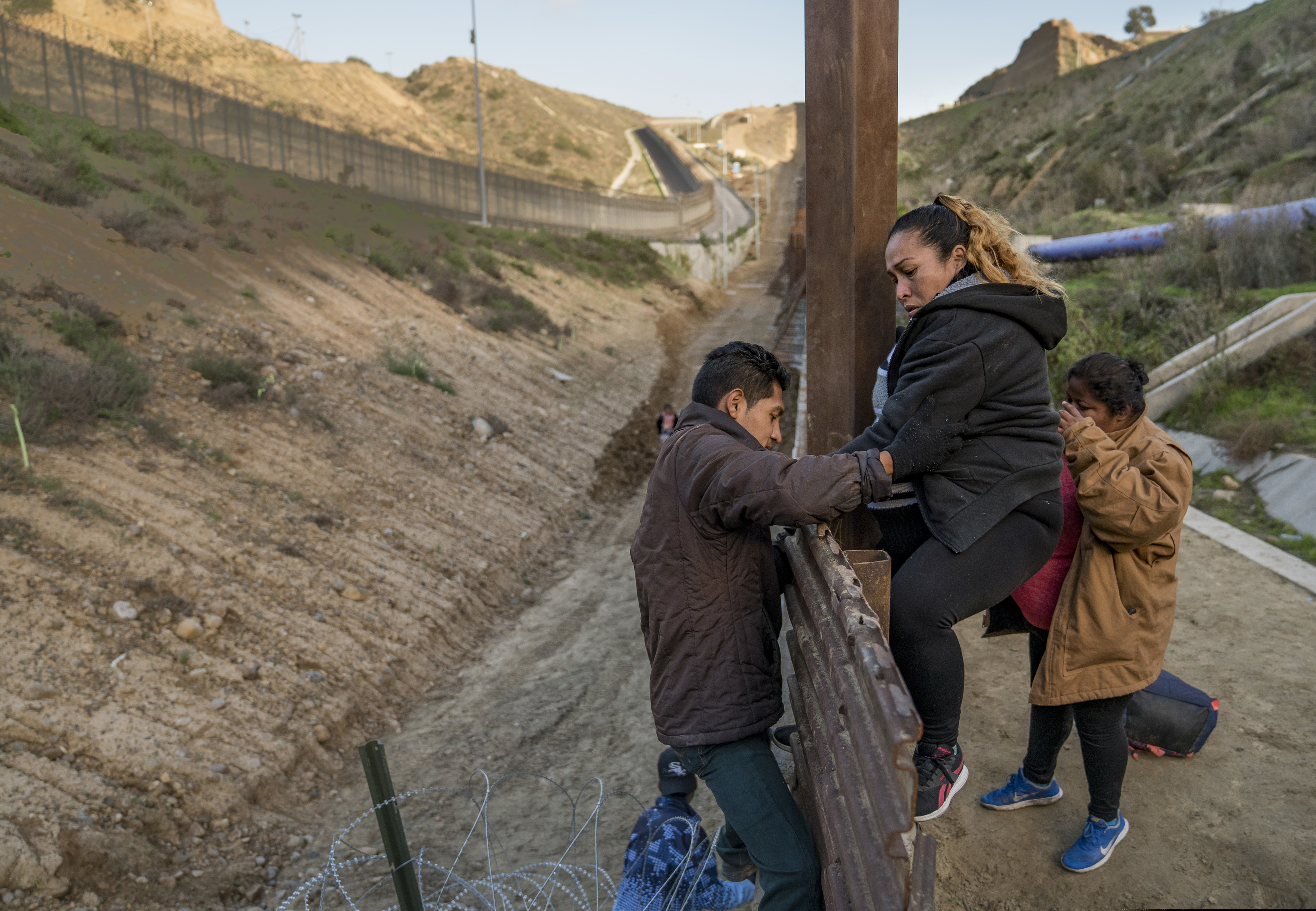 A pregnant migrant climbs the border fence before jumping into the U.S. to San Diego, Calif., from Tijuana, Mexico, Thursday, Dec. 27, 2018. Discouraged by the long wait to apply for asylum through official ports of entry, many Central American migrants from recent caravans are choosing to cross the U.S. border wall and hand themselves into border patrol agents. (AP Photo/Daniel Ochoa de Olza)