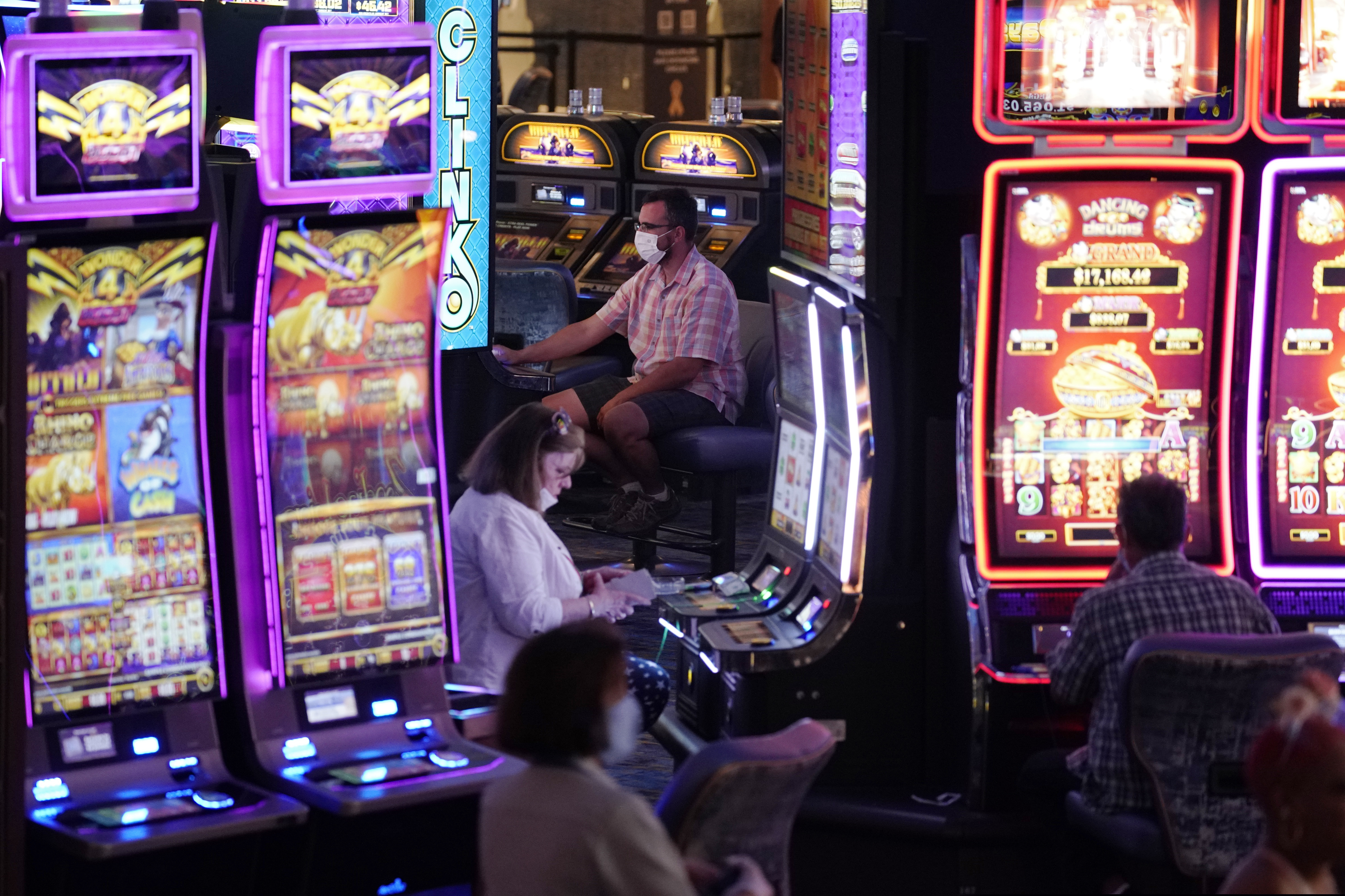 (John Locher | AP) In this July 4, 2020, file photo, people in masks as a precaution against the coronavirus play electronic slot machines on the Fourth of July at the Strat hotel-casino in Las Vegas. At least 123 visitors to Nevada tested positive for the coronavirus while visiting the state in recent weeks or shortly after returning home, according to state health data. The cases jumped in the weeks after Nevada's casinos reopened on June 4, 2020.